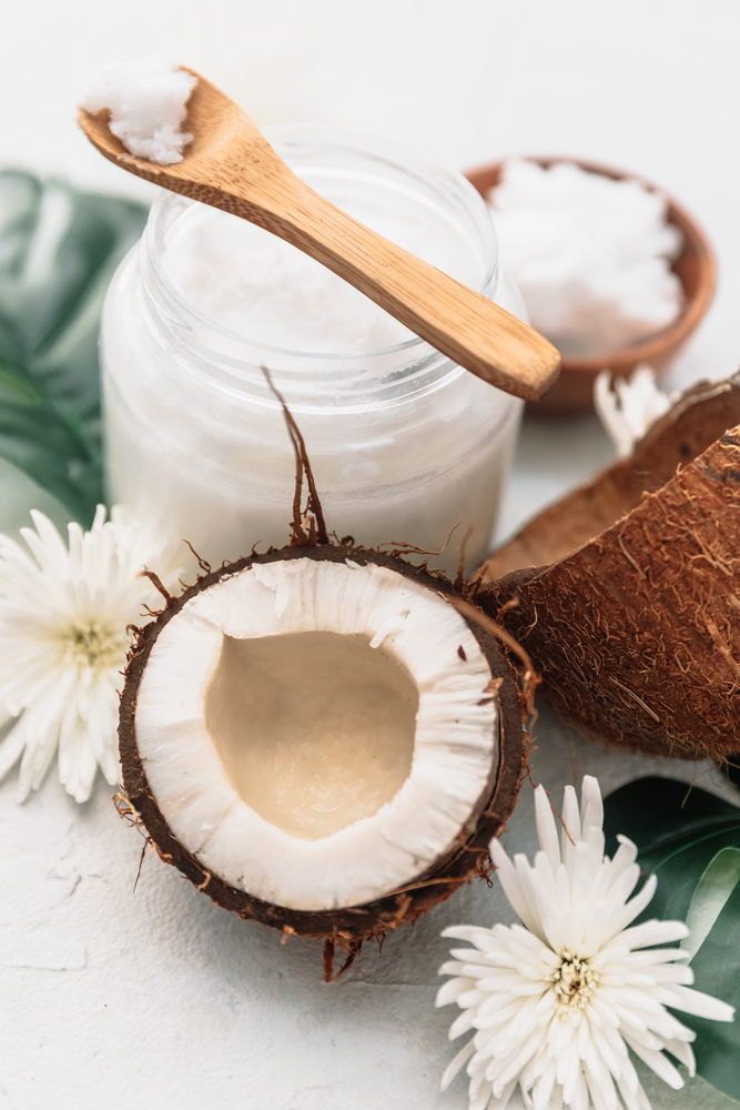 Organic healthy coconut butter in jar with fresh coconut pieces over on palm leaf on white background