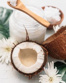 Organic healthy coconut butter in jar with fresh coconut pieces over on palm leaf on white background